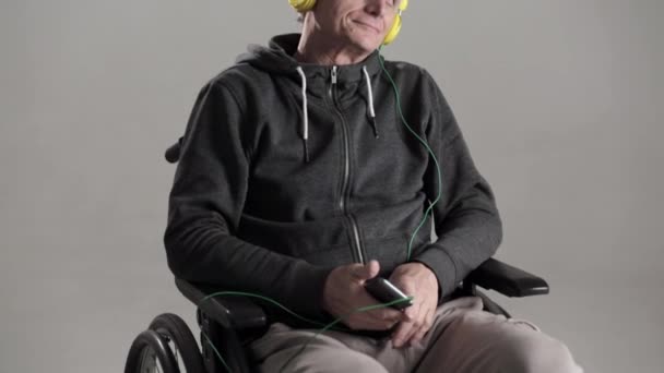 A Gray Haired Man in a Wheelchair Escucha Música Favorita con Auriculares . — Vídeo de stock