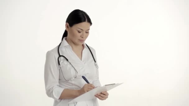 Asiatiska sjuksköterska på vit bakgrund ler och lyfter tummen. — Stockvideo