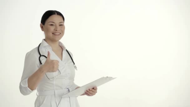 Asiático enfermeira no fundo branco sorrisos e elevadores polegar . — Vídeo de Stock