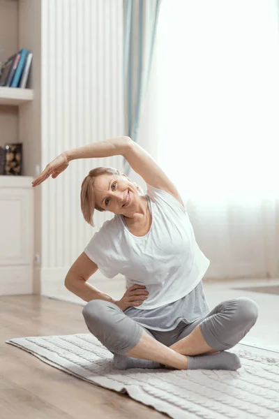 Evde yoga dersleri 50 yaş üzeri güzel kadınlar. — Stok fotoğraf