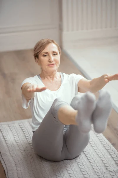 O femeie de peste 50 de ani care face yoga acasă în sufragerie . — Fotografie, imagine de stoc