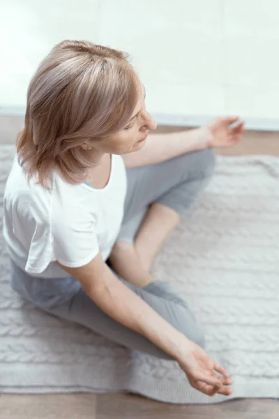 Una mujer mayor de 50 años hace yoga en casa . — Foto de Stock