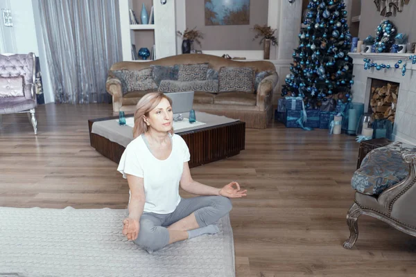 O femeie adultă meditează după ce face yoga acasă în camera de zi . — Fotografie, imagine de stoc