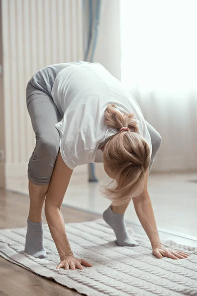 Donna dall'aspetto europeo sopra i 50 anni che fa yoga a casa in salotto . — Foto Stock