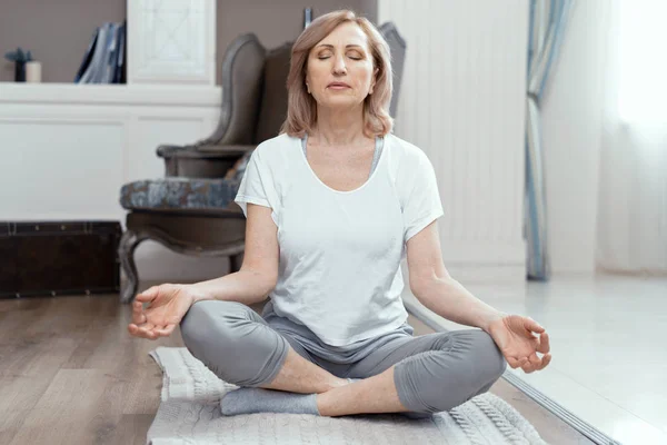 Una donna di età superiore ai 50 anni sta facendo yoga a casa . — Foto Stock