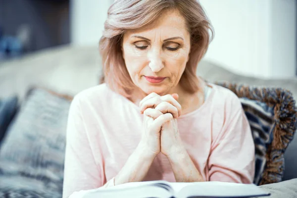 Женщина средних лет сидит на диване и молится — стоковое фото