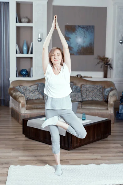 Una donna di 50 anni pratica yoga a casa in salotto . — Foto Stock