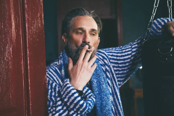 Un hombre de aspecto brutal con una barba fuma un cigarrillo después de tomar una ducha . — Foto de Stock