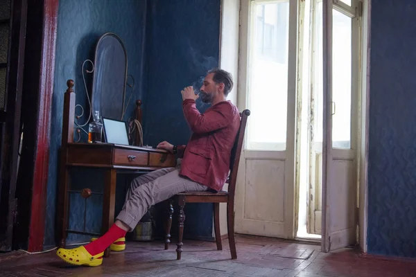 Hombre guapo trabaja en su portátil fumando y bebiendo — Foto de Stock