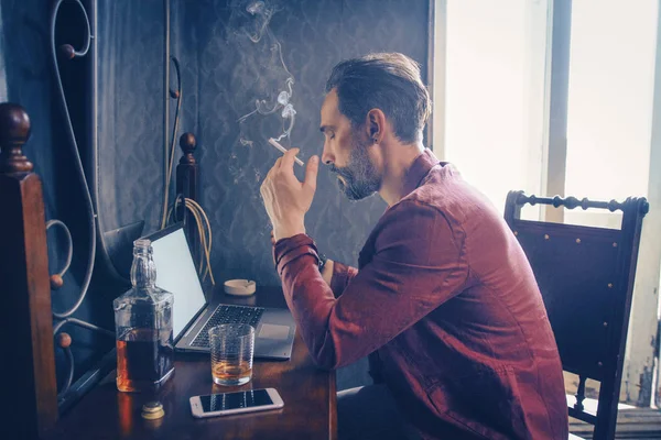 흡연과 음주 자신의 노트북에서 작동 하는 잘생긴 남자 — 스톡 사진