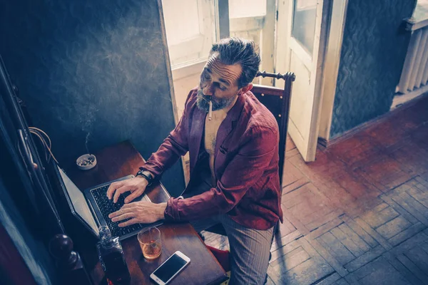 Bonito homem trabalha em seu laptop fumar e beber — Fotografia de Stock