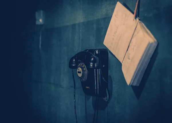 Vintage teléfono negro colgando en la pared junto a la que cuelga la guía telefónica . —  Fotos de Stock