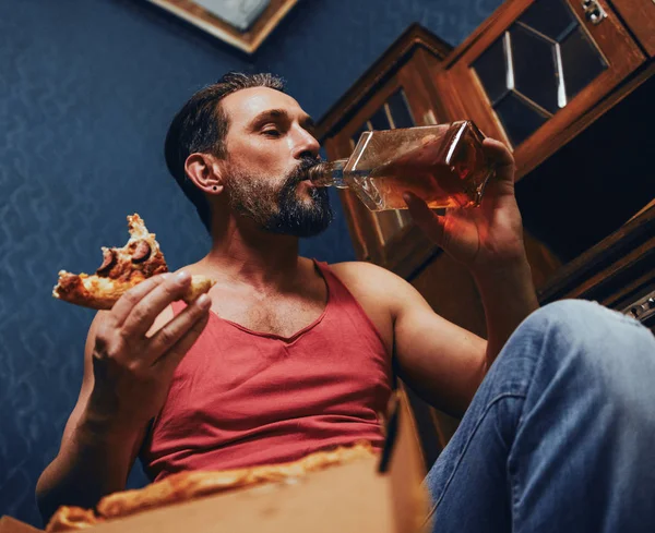 Brutal Bearded Man at Home Eating Pizza and Drinking Alcohol. — Stock Photo, Image