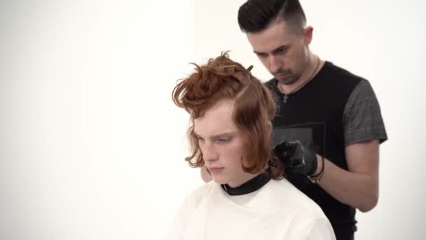 Barber holding a comb and scissor perfoming a haircut for a ginger client — Stock Video