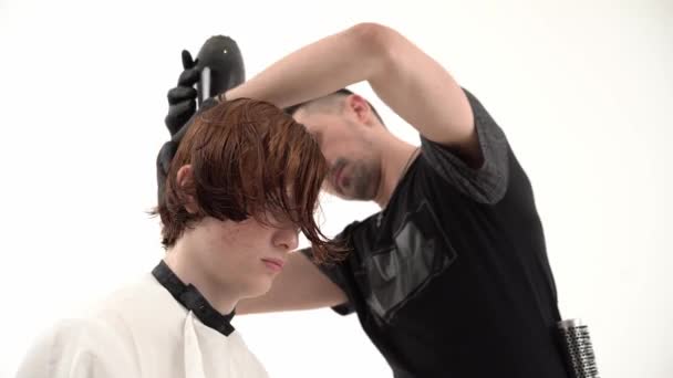 Barber with hairdryer drying and styling ginger hair of his client — Stock Video