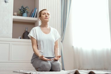 Attractive mature woman is practicing yoga in peace clipart