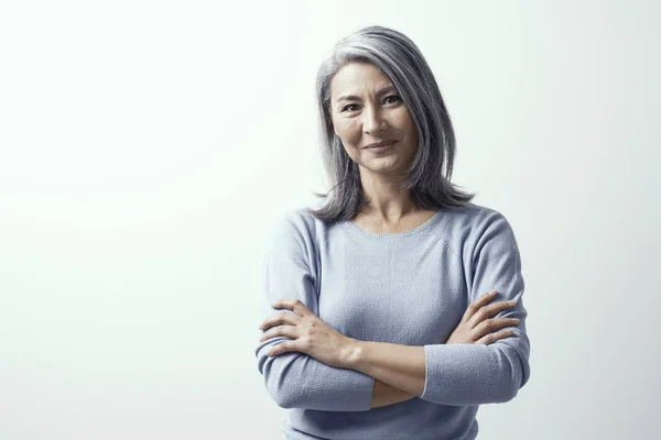 Mooie vrouw met grijs haar staande in de buurt van de muur handen gekruist — Stockfoto