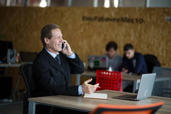 Un homme d'affaires bien habillé navigue sur son téléphone portable au bureau moderne, derrière une fenêtre, il est concentré et sérieux . — Photo