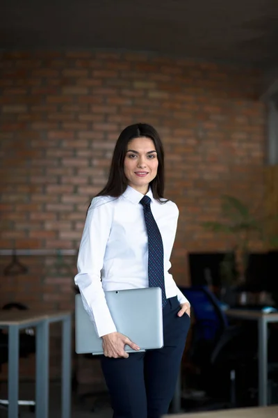 Smiling brunette businesswoman in business clothes holding laptop computer while looking at the camera and smiling. — Stock Photo, Image