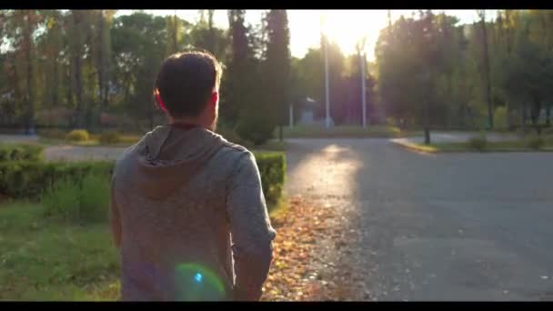 Спортивна людина біжить в зеленому осінньому лісі, освітленому сонцем — стокове відео