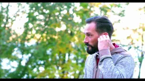 Hombre guapo de cabello oscuro está escuchando música en Summer Park — Vídeo de stock