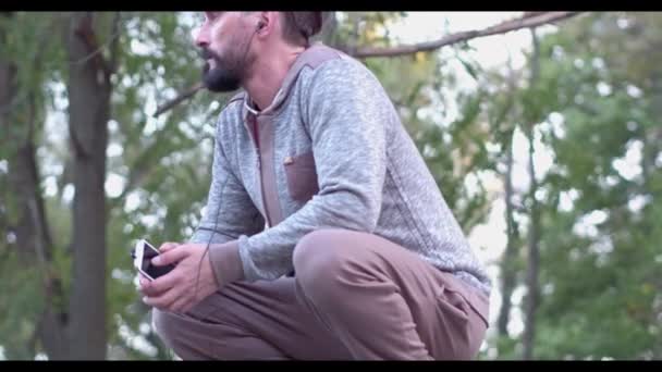 Krásný tmavovlasý muž poslouchá hudbu v letním parku — Stock video