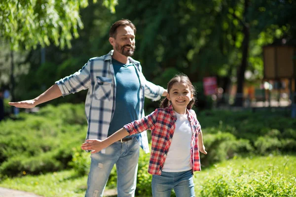 Far spenderar tid med dottern i parken medan Standind whith vilda öppnade händer och leende. — Stockfoto