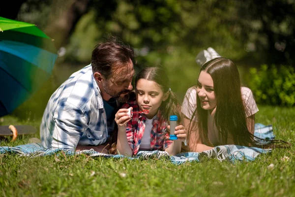 Rodzina leżąca na kocu w parku. Córka Holding mydło Bubbles. — Zdjęcie stockowe