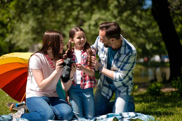 Nuori nainen näyttää kuvia miehelleen ja tyttärelleen istuessaan huopalla puistossa . — kuvapankkivalokuva