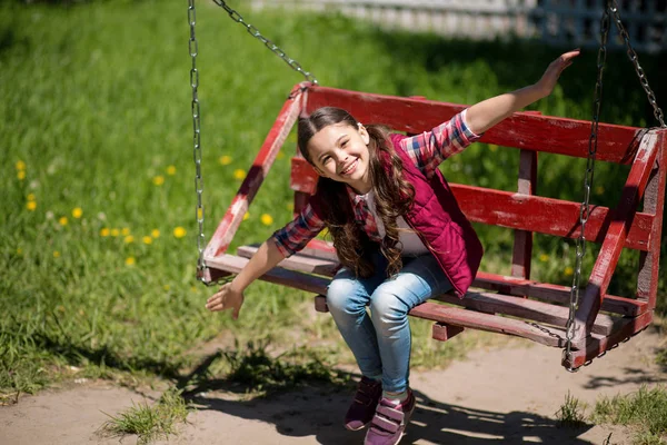 Uśmiechnięta dziewczynka z długimi warkoczami jest na huśtawce w parku. — Zdjęcie stockowe