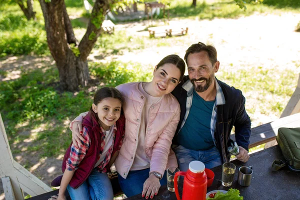 Lycklig familj sitter på bänken i lusthus i parken och leende. — Stockfoto