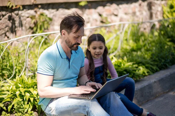 Vader Siting samen met zijn dochter en kijken op de laptop buitenshuis. — Stockfoto