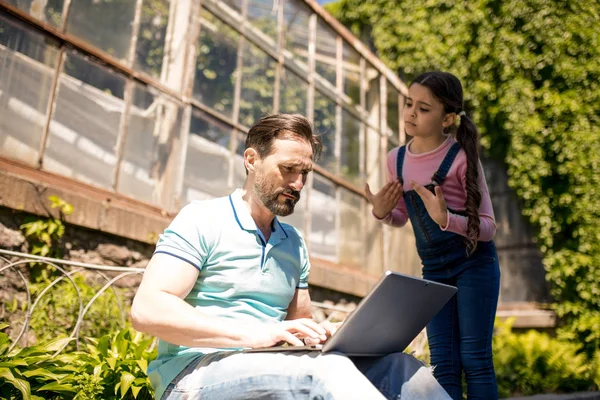 Dochter probeert vaders aandacht te trekken terwijl ze buiten staat. vader typt op zijn laptop. — Stockfoto