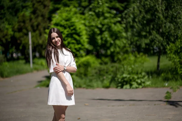 Junge lächelnde brünette Frau im Park berührt ihre rechte Hand mit ihrer linken Hand. — Stockfoto