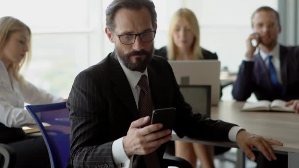 Líder del equipo de negocios se burla de su móvil y sonríe a la cámara — Vídeo de stock