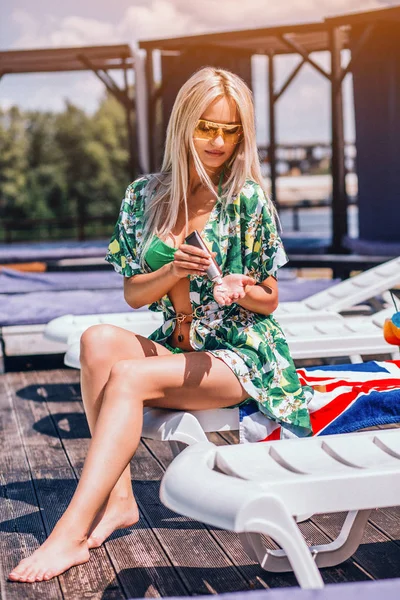 Sexy Frau sitzt im grünen Siegeranzug auf dem Liegestuhl am Pool. — Stockfoto