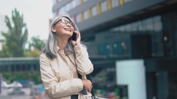 Die Asiatin mittleren Alters lächelt und spricht auf ihrem Smartphone — Stockvideo