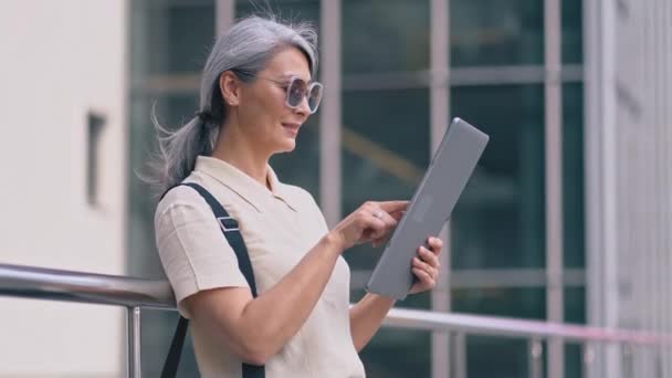 Die asiatische Geschäftsfrau steht mit einem Tablet-Computer vor dem Bürogebäude — Stockvideo