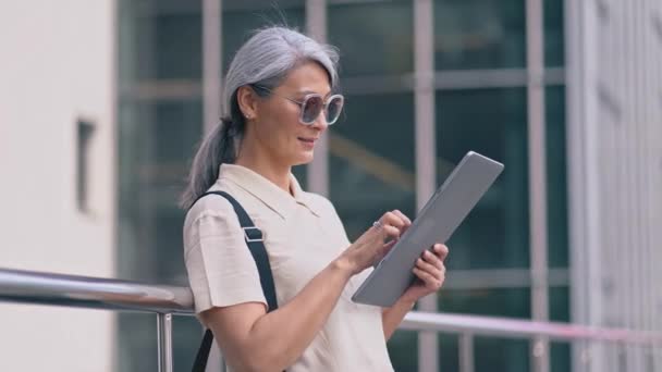 De Aziatische zakenvrouw staat met een tablet computer in het kantoorgebouw — Stockvideo