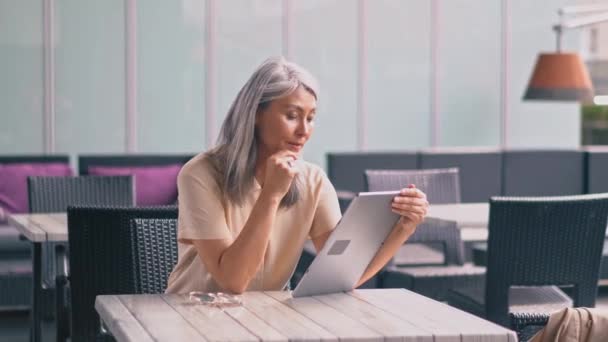 Dobře vypadající asijská žena středního věku sedí v kavárně a pracuje na tabletu — Stock video