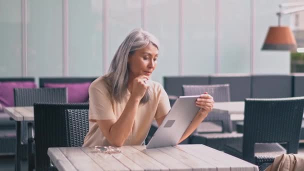 De mediana edad hermosa mujer asiática está sentado en el café y trabajando en la tableta — Vídeos de Stock