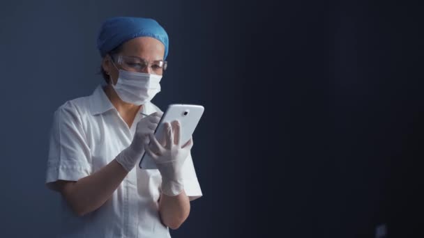 Koruyucu maske takan ve üniformalı bir doktor elinde tutuyor. Hastanın yeni verileri sunduğu tablet düzenleme bilgileri. Sağlık konsepti. Prores 422 — Stok video