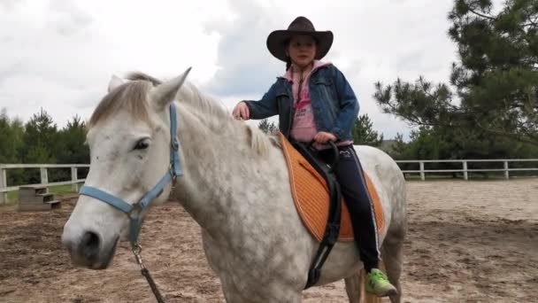 Bambina col cappello da cowboy che impara a cavalcare. Trainer cambia il cappello sul casco da allenamento come protezione. Concetto di ranch. Marzo 2020. Kiev, Ucraina. Prore 422 — Video Stock