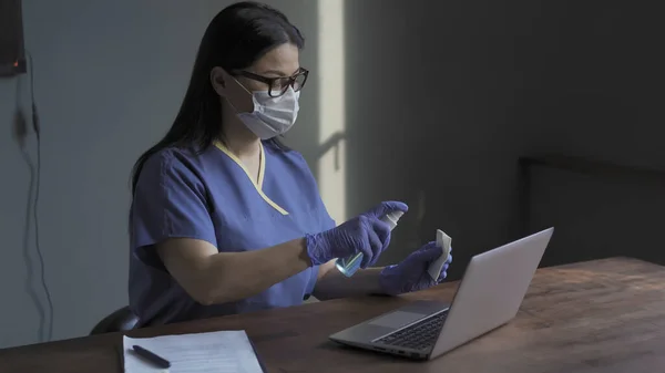 Médico feminino computador portátil de limpeza com spray anti-séptico. Mulher limpa o teclado de um computador portátil com um spray anti-séptico e guardanapo enquanto está sentado à mesa em seu escritório — Fotografia de Stock