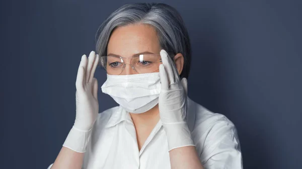 O doutor no uniforme ajusta copos de segurança. Mulher branca bonito usando máscara protetora e luvas descartáveis ajusta seus óculos. Fecha o retrato. Imagem tonificada — Fotografia de Stock