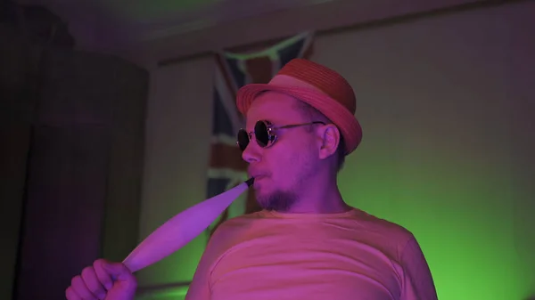 Hipster w okularach przeciwsłonecznych człowiek dymiący hookah siedzi w domu w jasnych kolorach neonów. Na brytyjskiej fladze ciemne tło. Koncepcja stylu życia — Zdjęcie stockowe