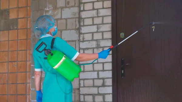 Vrouw in uniform met een antiseptische ballon die buiten werkt. Medische professional verwerkt de voordeur met desinfecterende oplossing. Achteraanzicht. Stadsziekenhuis. mei 2020, Brovary, Oekraïne — Stockfoto