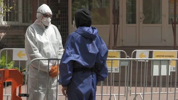 Gele gang bij ziekenhuisingang. De man in epidemiologisch pak communiceert met de bewaker over het hek. Officieel centrum van tegenactie covid-19. Stadsziekenhuis. mei 2020, Brovary, Oekraïne — Stockfoto