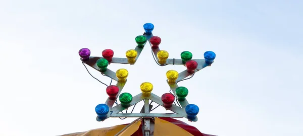 Sternförmige Lampe am Karusselldach gegen den Himmel. Beleuchtung mit bunten Glühbirnen am sonnigen Tag — Stockfoto