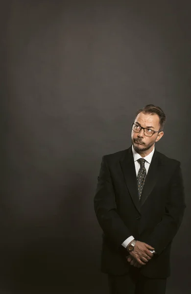 Homme d'affaires réfléchi attend debout avec les mains jointes et regardant vers le haut contre le mur gris arrière. Modèle pour idées d'entreprise, schémas et diagrammes. Contexte de la créativité et des croquis. Image tonique — Photo